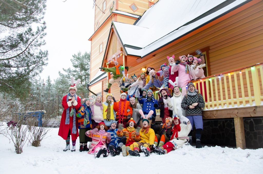 Gruppo con personaggi in costume davanti a una casa in legno innevata a Lottemaa.