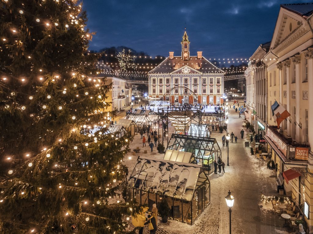 Albero di Natale illuminato in primo piano e mercatino nella piazza del Municipio di Tartu.