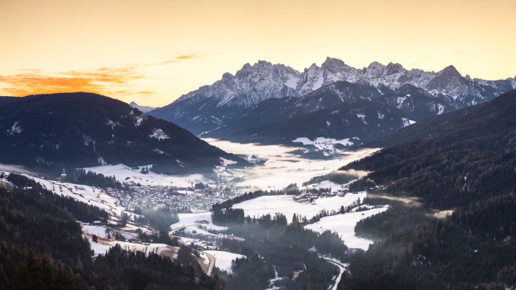 Panorama delle Dolomiti innevate all'alba, con un paese nella valle
