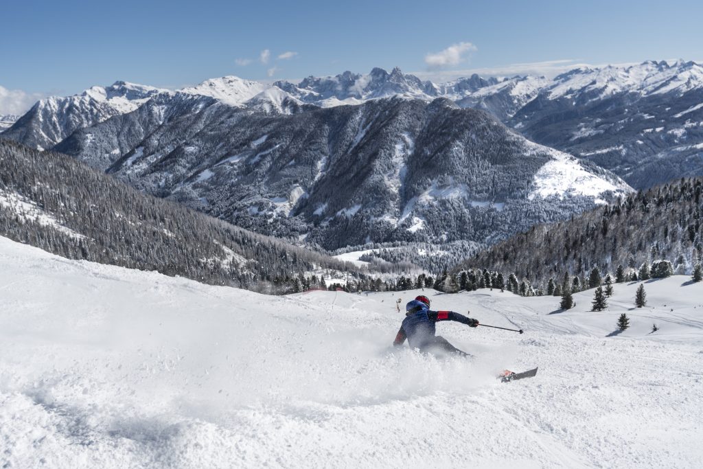 Sciatore in curva solleva neve durante una discesa nello Ski Center Latemar.